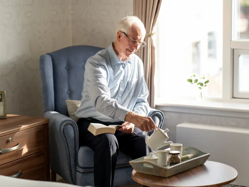 A resident enjoying afternoon tea in a sunlit lounge at Cramond Residence